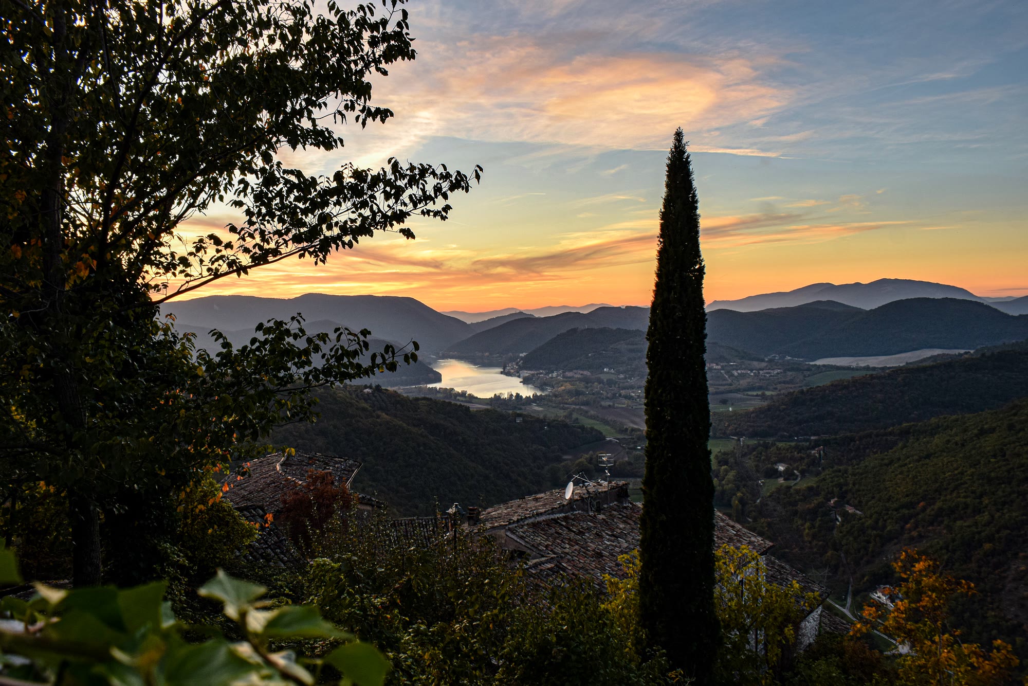 Cypress tree and green hills above a lake at sunset in central Italy