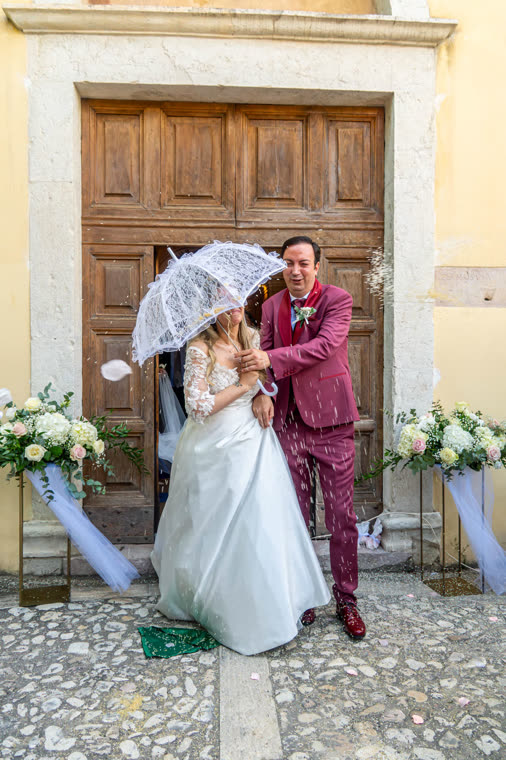 Sposi con l'ombrellino di pizzo davanti al portone della chiesa